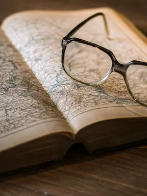 Antique book open to a map with eyeglasses on top, evoking exploration.