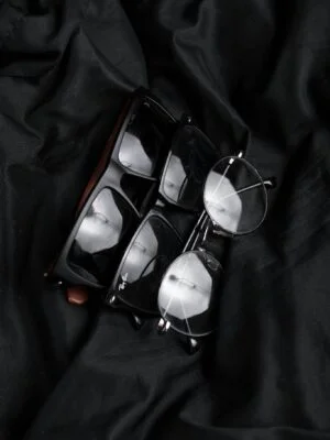 Close-up of various stylish eyeglasses on black fabric, highlighting modern eyewear design.