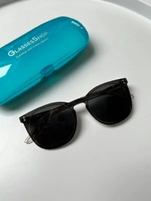 Elegant black sunglasses with a blue case on white surface, perfect for modern summer fashion.