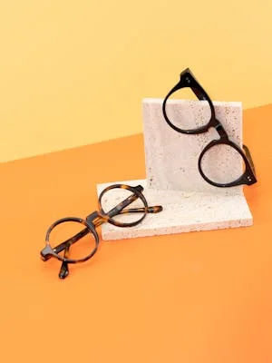 Stylish round eyeglasses on a minimalist concrete and colorful backdrop.