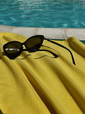 Stylish sunglasses resting on a vibrant yellow towel by a pool, capturing a relaxing summer vibe.